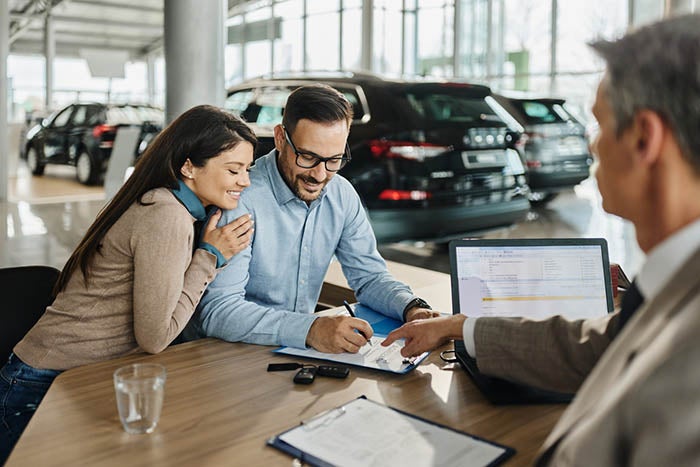  A couple is signing a contract regarding car payments at the car dealership.