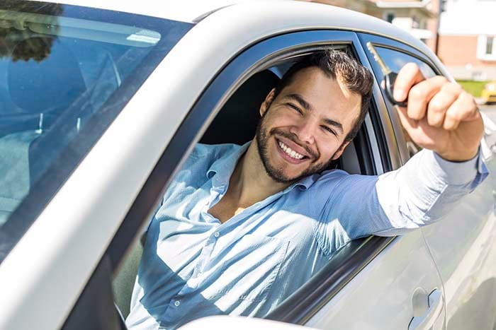 A cheerful and joyful man inside the car is holding his keys for his new car, he just refinanced his car loan