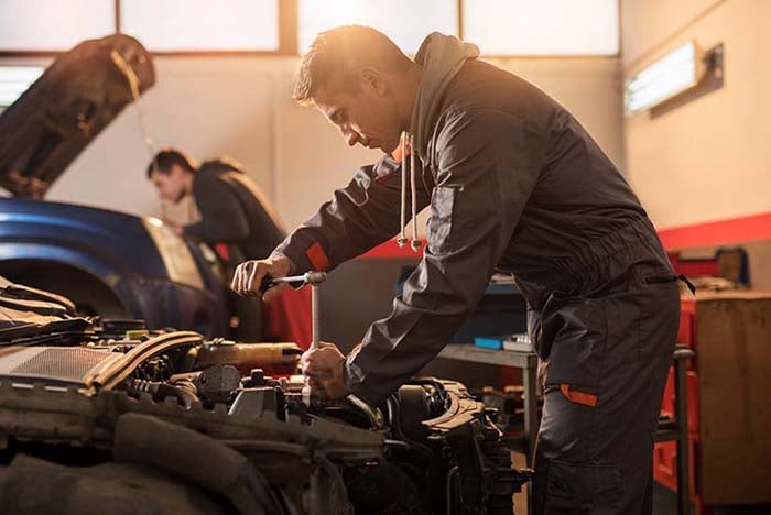 The auto mechanic is diligently working on truck maintenance, specifically focusing on the engine, in the repair shop. Tightening the nut bolt on the truck for safer use
