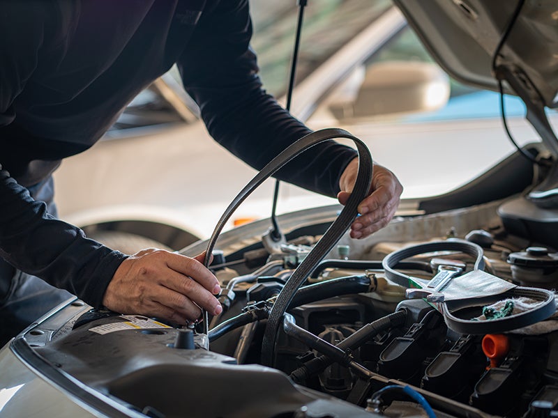 Two auto mechanics in branded uniforms, a man and a woman, review diagnostics on a tablet near a raised car.