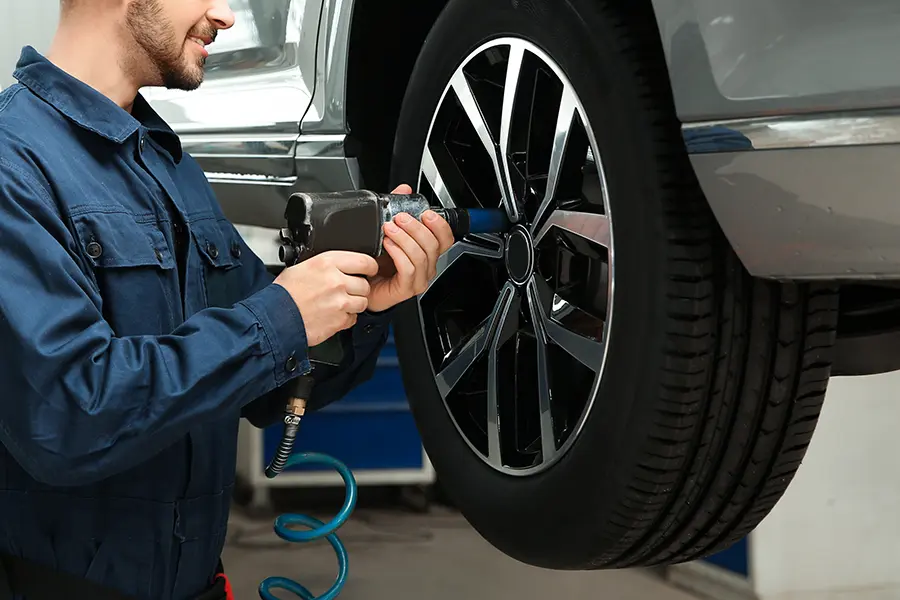 A Ford service technician in a blue and gray uniform, leaning over an open car hood and working under it.